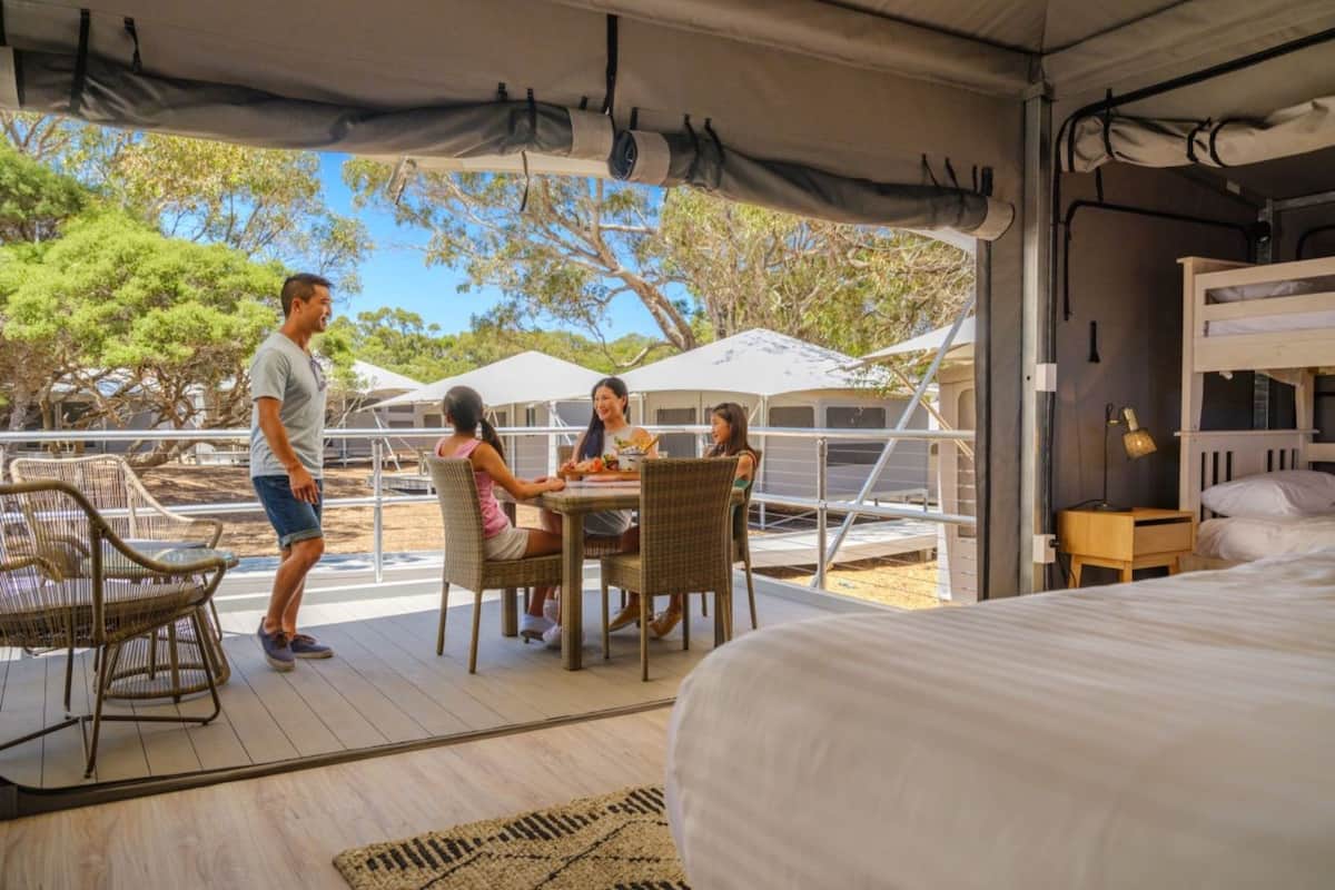 A tented accommodation with a dining area, a bed, and a view of trees.