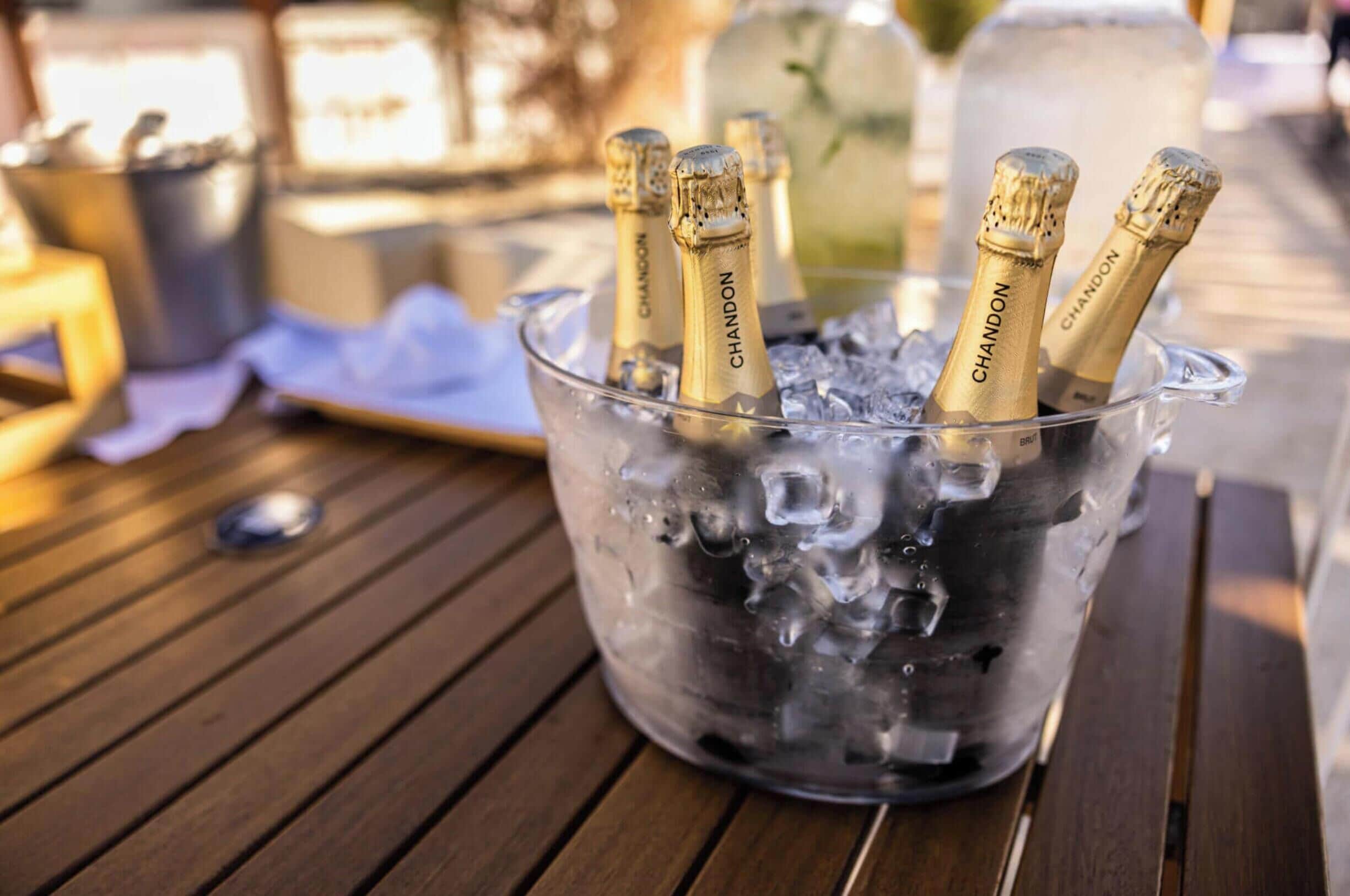 A glass container filled with ice and champagne bottles labeled "CHANDON" on a wooden table.