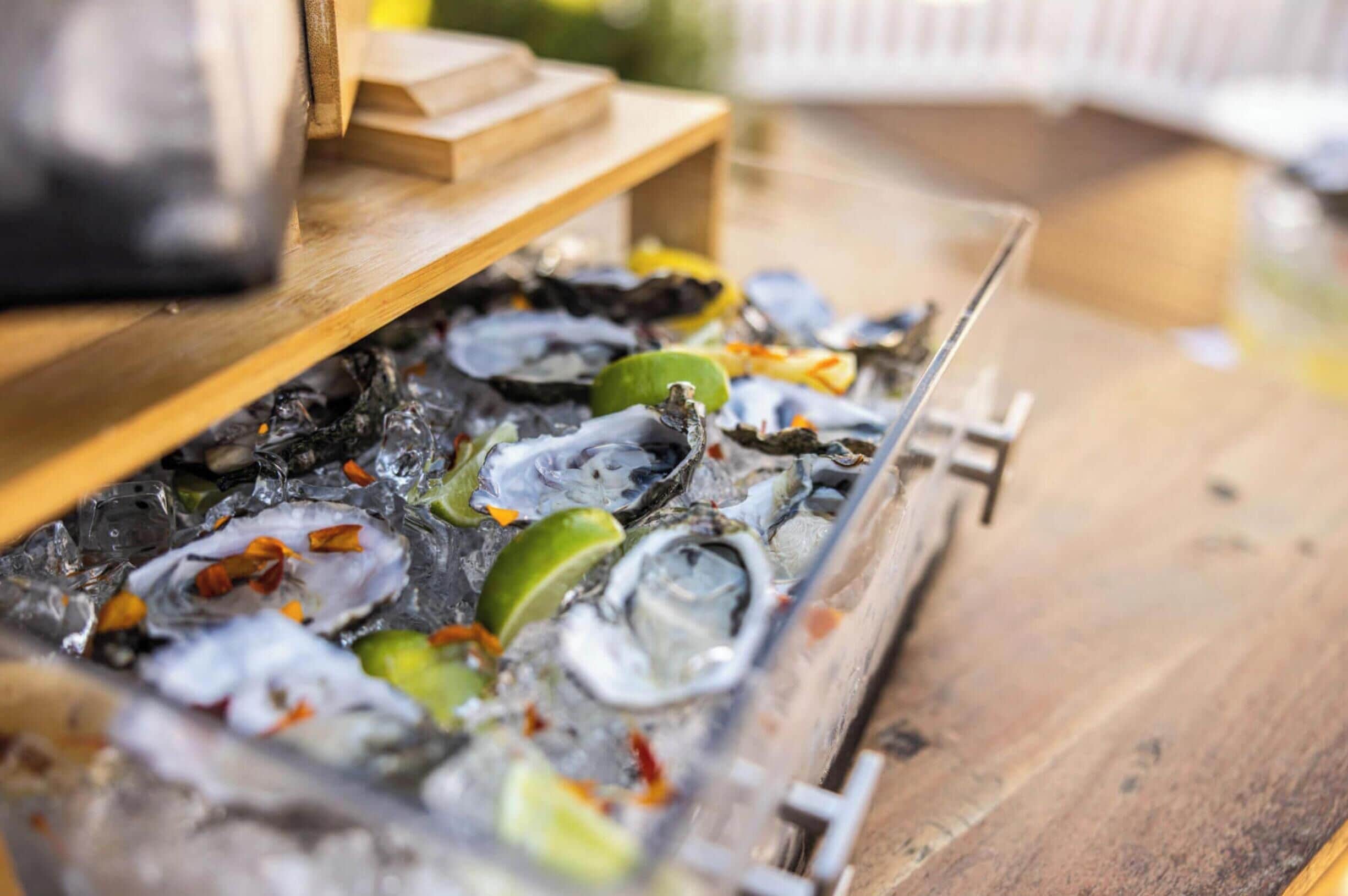 A tray of oysters on ice with lime wedges and a wooden tray.