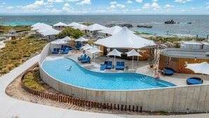 A pool area with lounge chairs and umbrellas, surrounded by buildings with a view of the ocean.
