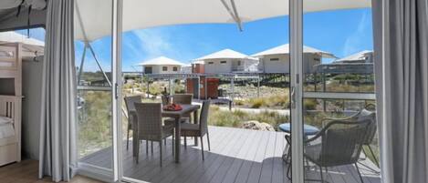 A balcony with a table and chairs, a view of a beach, and a building in the background.