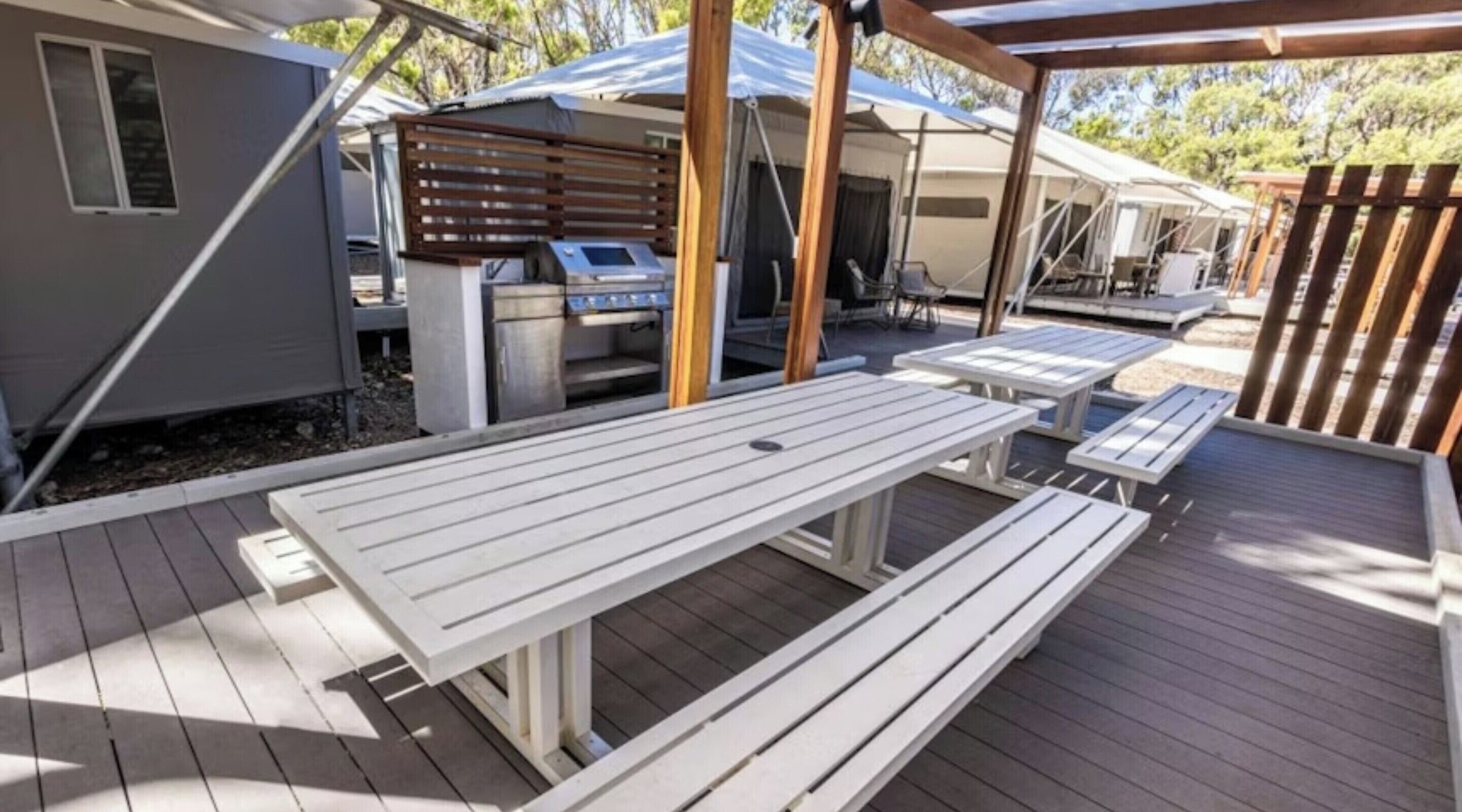 Una terraza con mesas de picnic, una parrilla y un área cubierta con una mesa y sillas.