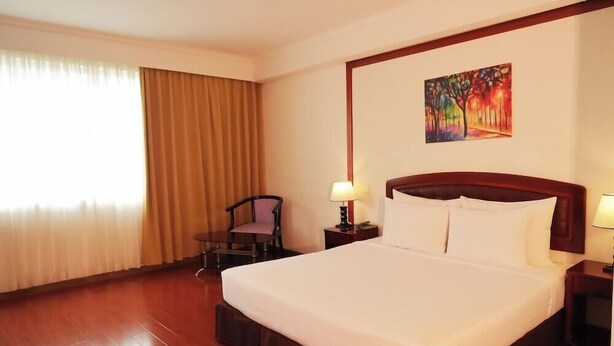 Una habitación de hotel con una cama grande, una silla, un cuadro en la pared y una ventana con cortinas.