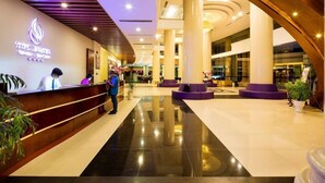 Um hall de hotel com balcão de recepção, colunas imponentes e design moderno.