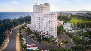 Un hotel de varios pisos con un patio central, rodeado de vegetación y vistas al mar.