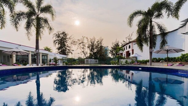 Piscina com reflexos nítidos, cercada por palmeiras e edifícios modernos.