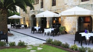 An outdoor dining area with tables and chairs under umbrellas, set against a stone building with arches. - LOS Guardeses (Medio Cudeyo)