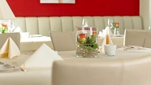 A dining area with a red wall, a white cushioned bench, and a table set with white tablecloths and napkins. - Hotel Restaurant Sengscheider Hof (Sankt Ingbert)