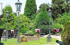 An outdoor seating area with tables and chairs, surrounded by greenery and lamp posts. - Hotel Restaurant Sengscheider Hof (Sankt Ingbert)