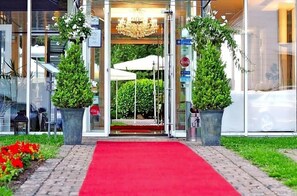 A hotel entrance with a red carpet, glass doors, and potted plants.