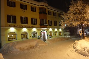 Un bâtiment d’hôtel appelé « Gasthof GOLDENER FISCH », doté de nombreuses fenêtres et d’une entrée recouverte de neige.