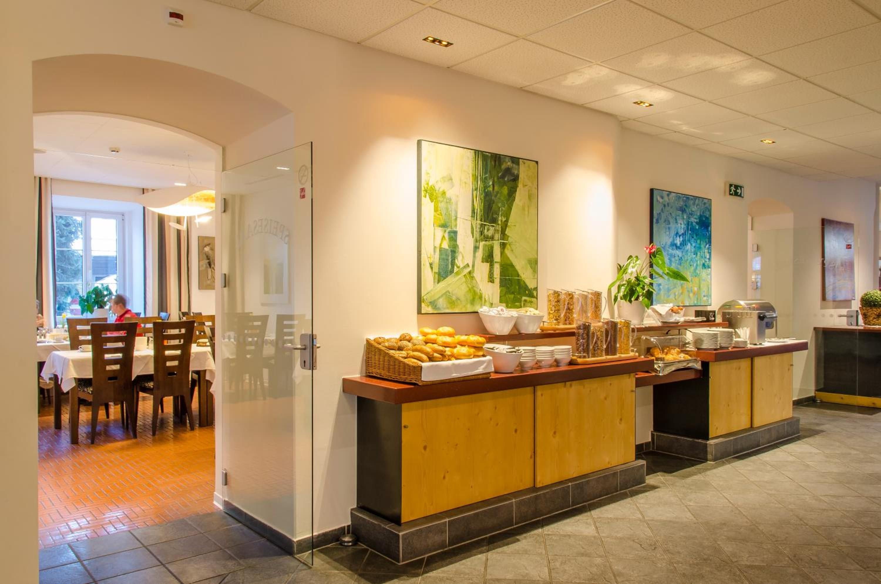 Eine Hotelhalle mit Selbstbedienungsbereich, Esstischen und Kunstwerken an den Wänden.