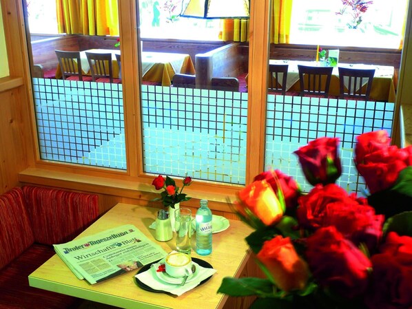 A dining area with a table set for two, a newspaper, a bottle, and a vase with flowers.