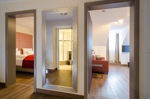A hotel room with a large mirror, a bed with red bedding, a red sofa, and a small table.