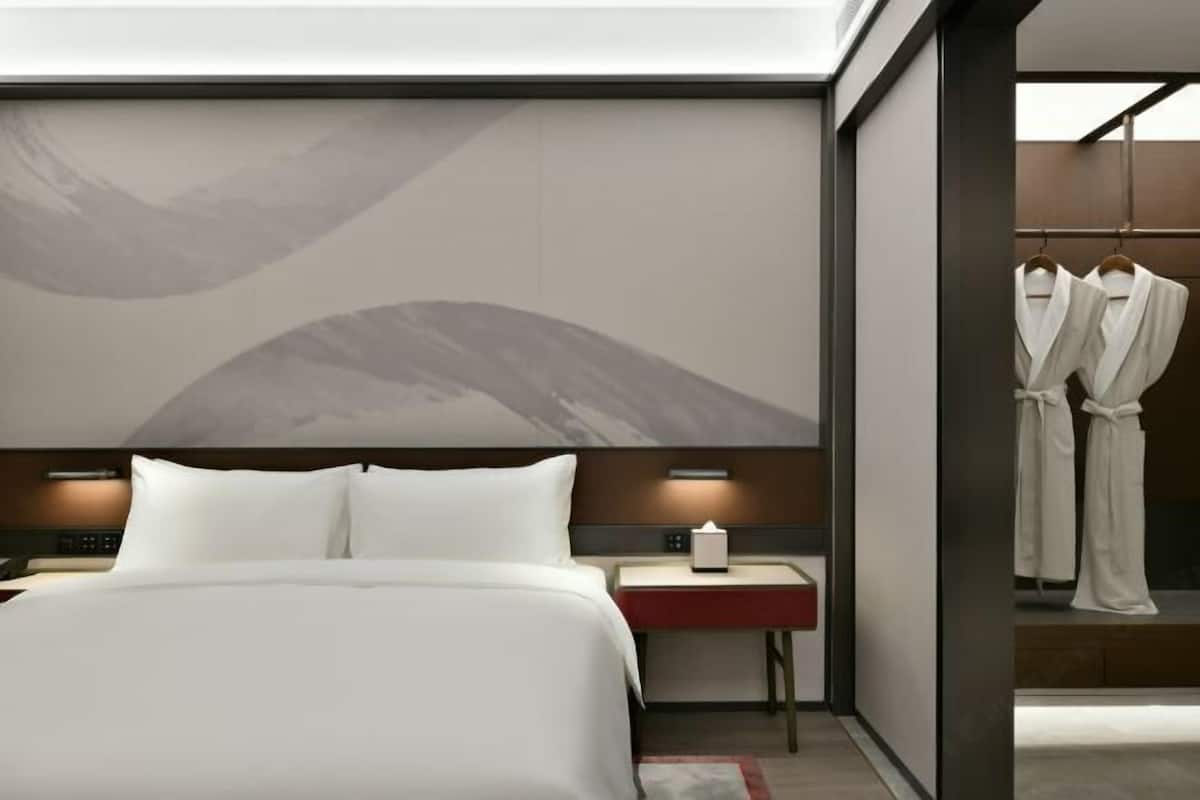 Una habitación de hotel moderna con una cama grande, mesitas de noche, un perchero para bata y una obra de arte colgada en la pared.