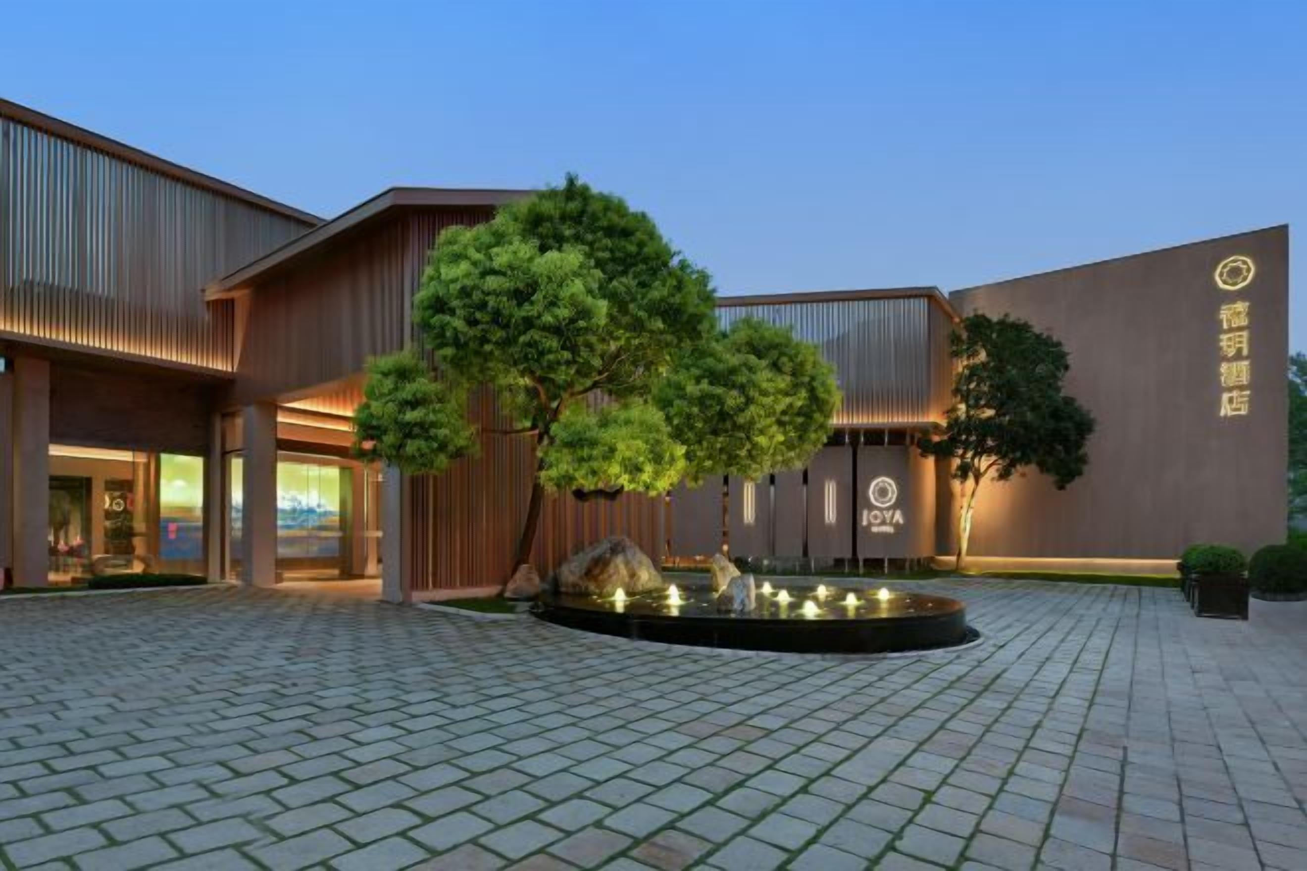 A modern building with a courtyard, a large tree, and a sign indicating a hotel.