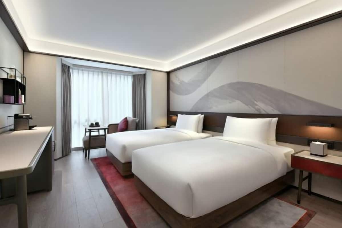 Habitación de hotel con dos camas, un escritorio, una silla, una mesita y un cuadro abstracto grande en la pared.