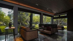 A modern interior with a glass partition, leather sofas, a small table, and a view of a garden. - JOYA Hotel Jia Ding (Shanghai)