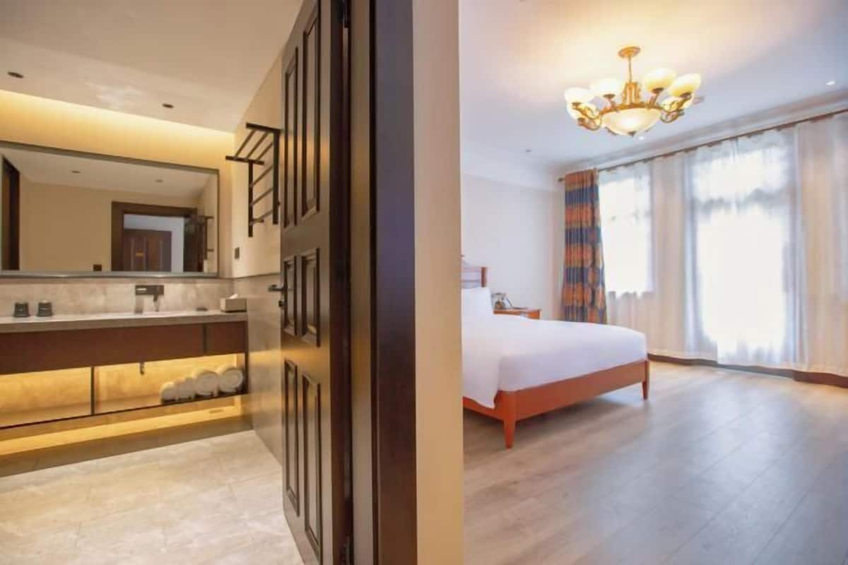 Habitación de hotel con una cama grande, baño con tocador y candelabro.