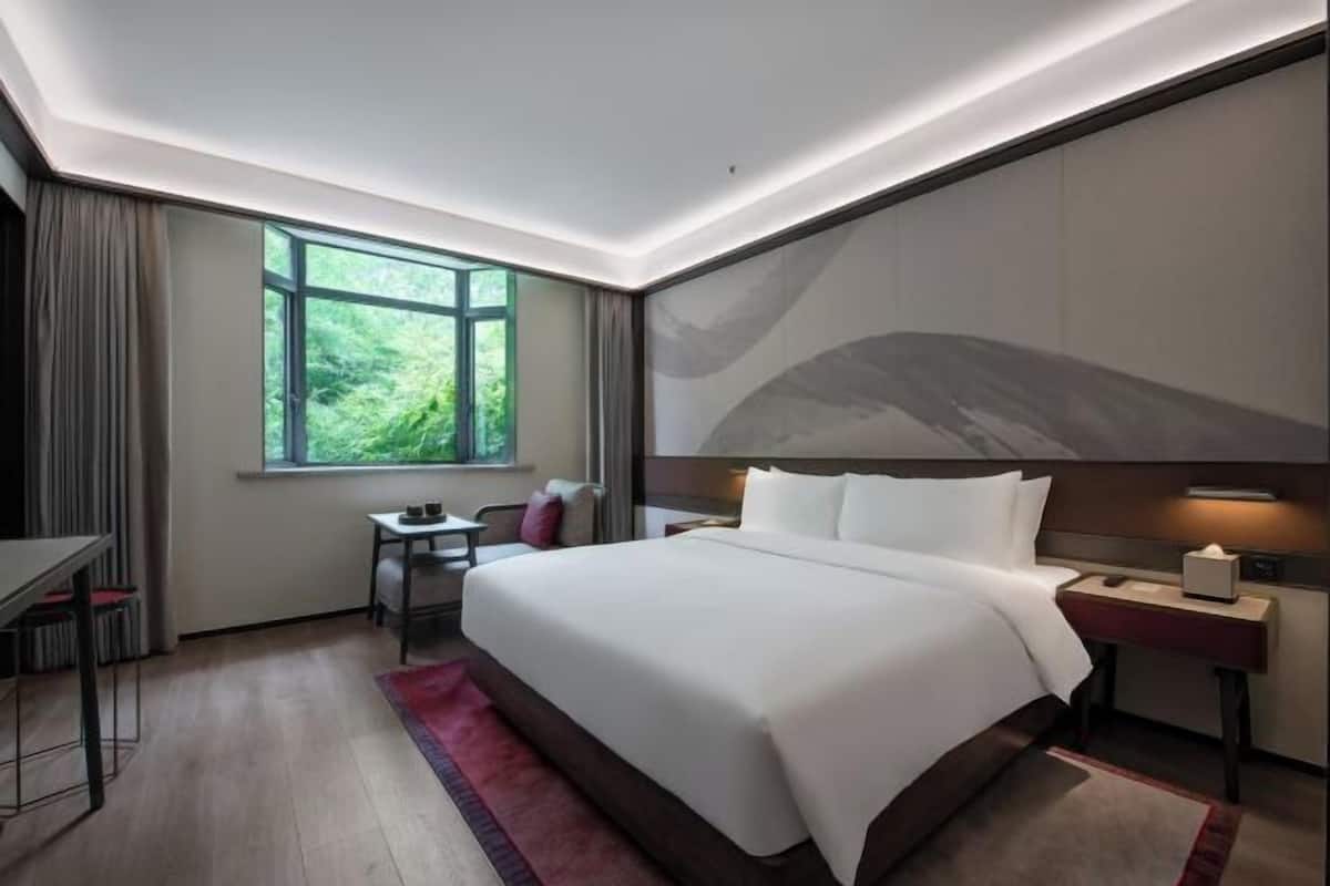 Una habitación de hotel moderna con una cama grande, un escritorio y un ventanal con vistas a zonas verdes.