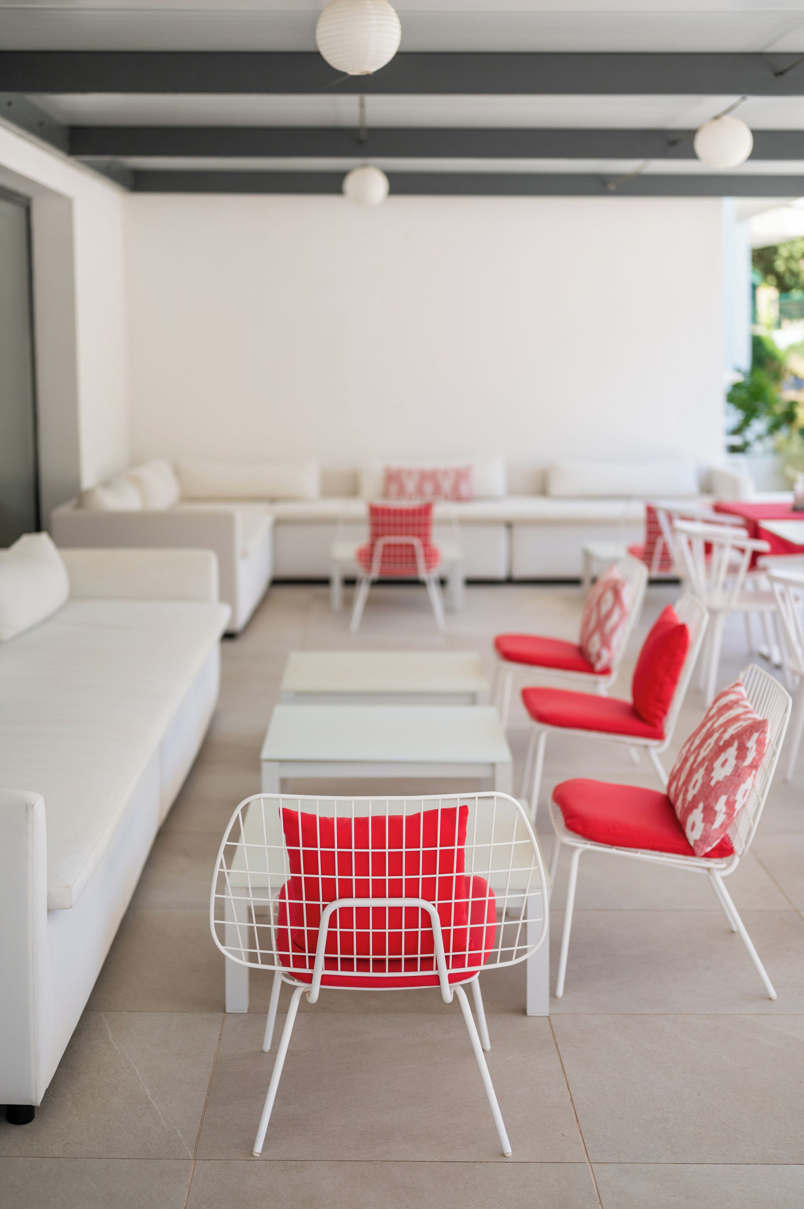 A modern outdoor seating area with white sofas and red and white chairs.