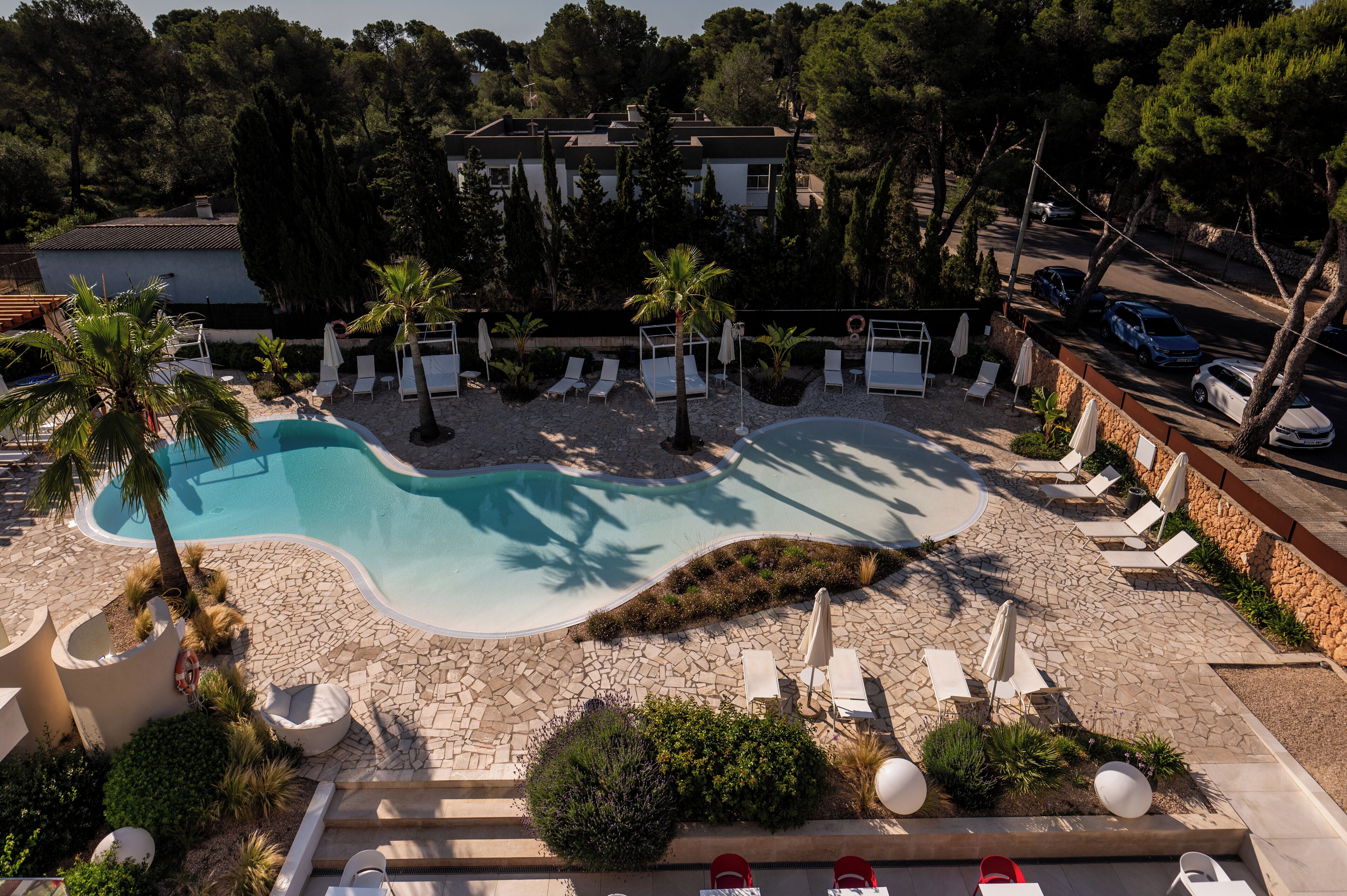 Un espace piscine agrémenté de chaises longues et de parasols, entouré d’une terrasse en pierre et de verdure.
