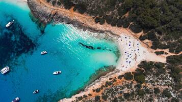 Vista aérea de una zona costera con playa arenosa, aguas turquesas cristalinas y varios barcos.