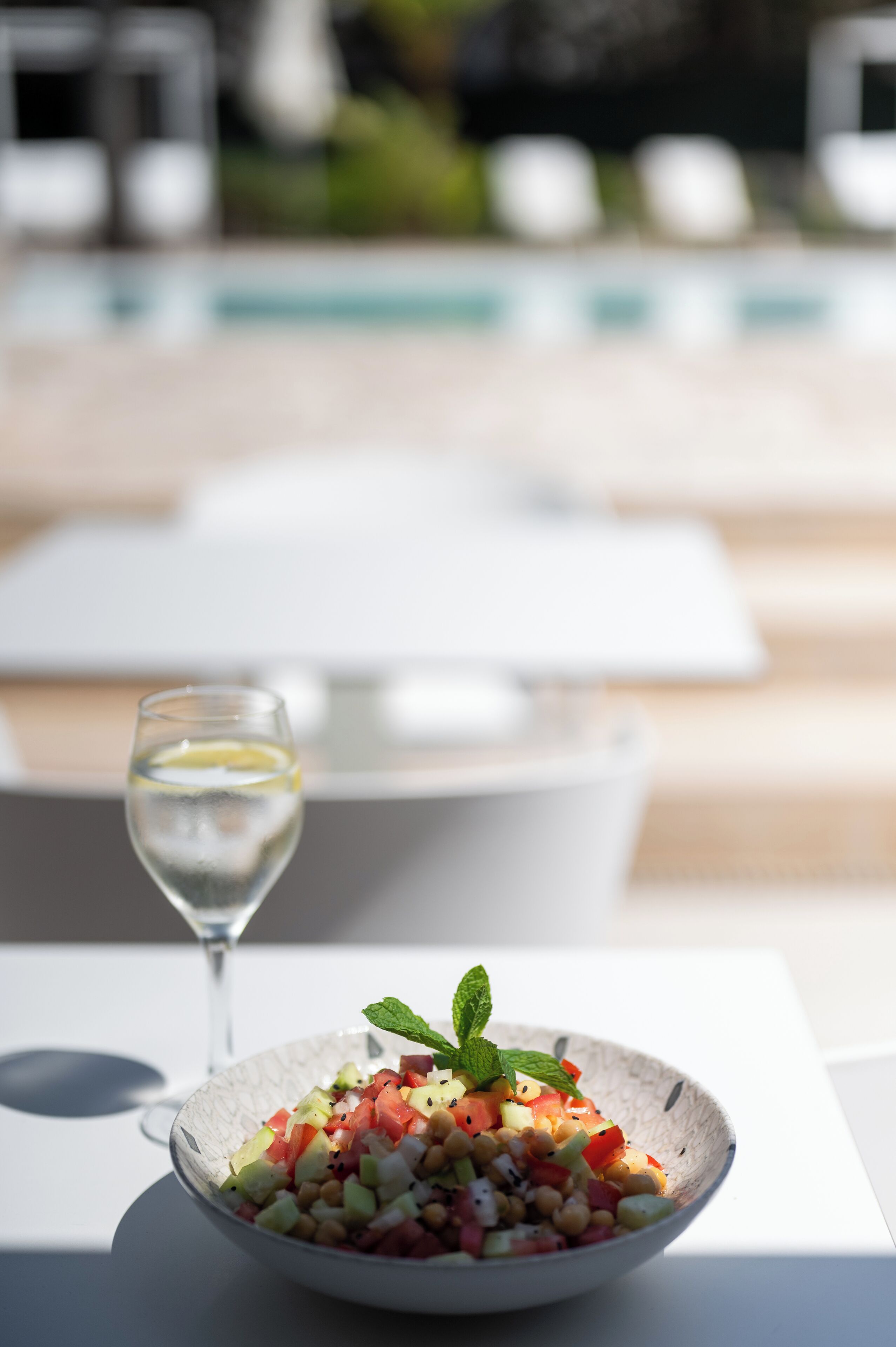 A bowl of fruit salad with a mint garnish on a table by a poolside.