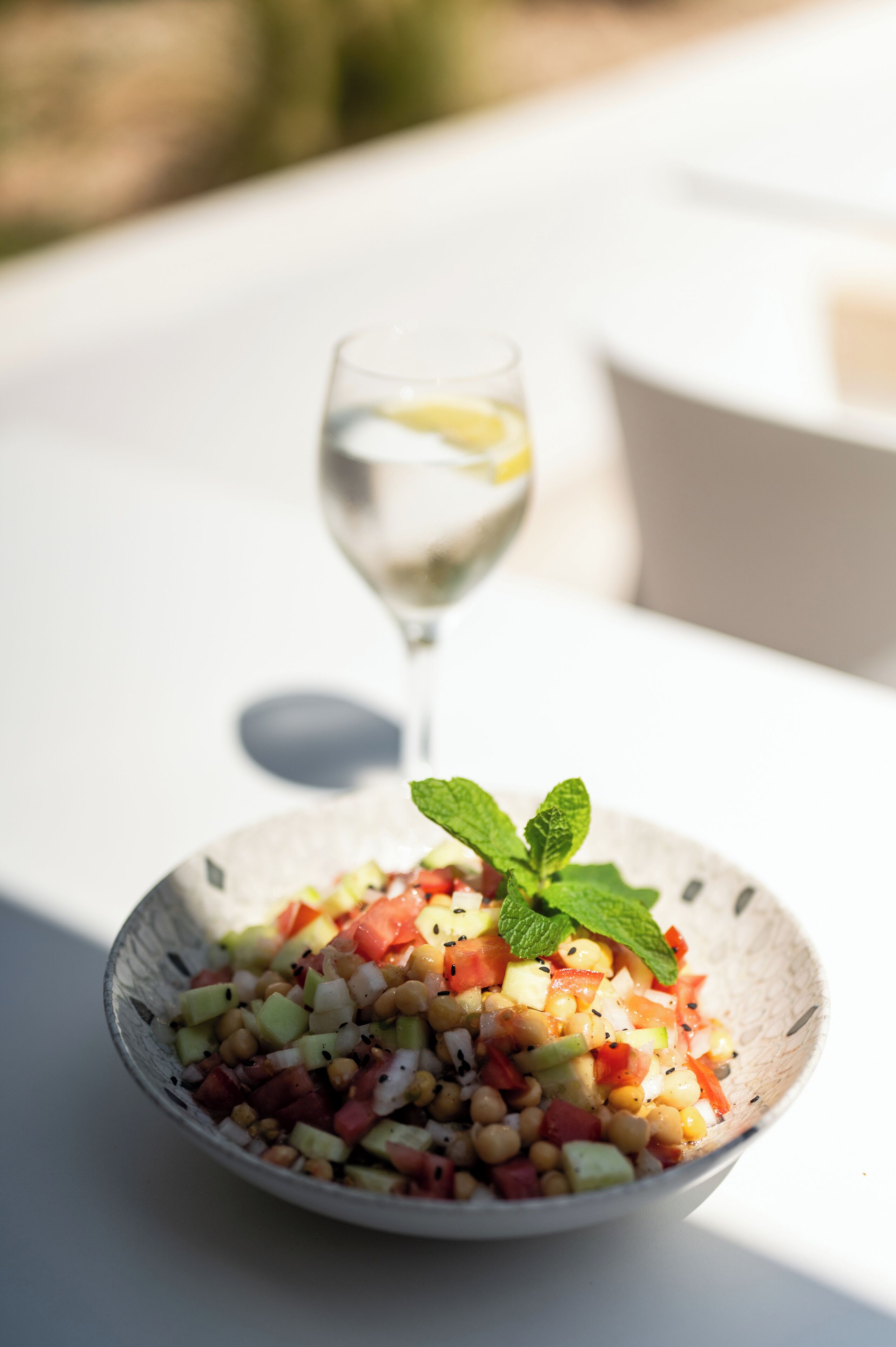 A bowl of salad with a mint garnish on a white table.