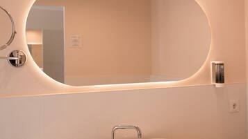 A modern bathroom with a round mirror, a vessel sink, and neatly rolled towels on the counter.