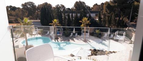 Un balcon avec une piscine, des chaises blanches et une table.