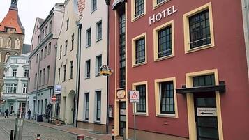 Ein Hotelgebäude mit roter Fassade und gelben Fensterrahmen, eine Kopfsteinpflasterstraße sowie ein Kirchturm im Hintergrund.