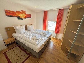 A hotel room with two beds, a wardrobe, and a window with curtains.