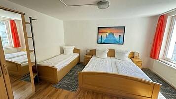 A hotel room with a large bed, two smaller beds, a wardrobe, a painting, and a window with curtains.