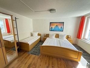 A hotel room with a large bed, two smaller beds, a wardrobe, a painting, and a window with curtains.