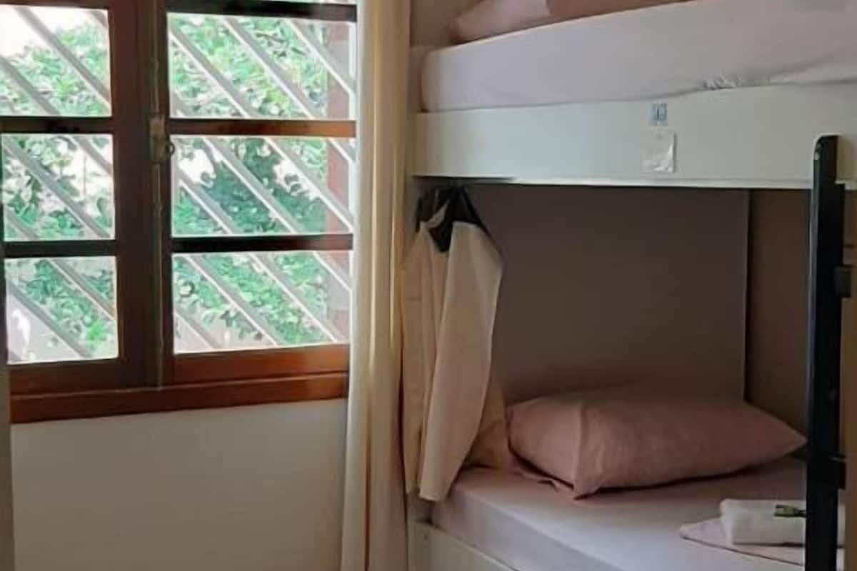 A bunk bed room with a window, a small stool, and a wardrobe.