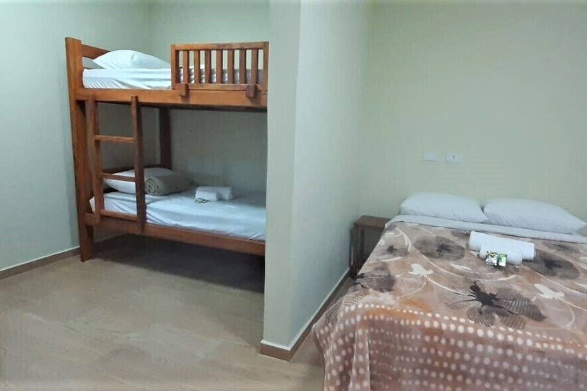 A room with a bunk bed, a single bed, a small table, and a nightstand.