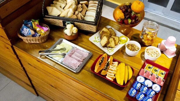 A buffet table with various food items including bread, fruits, and condiments. - Hostel B2B (São Paulo)