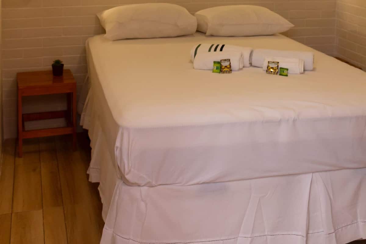 A neatly made bed with pillows and a small bedside table with a plant.