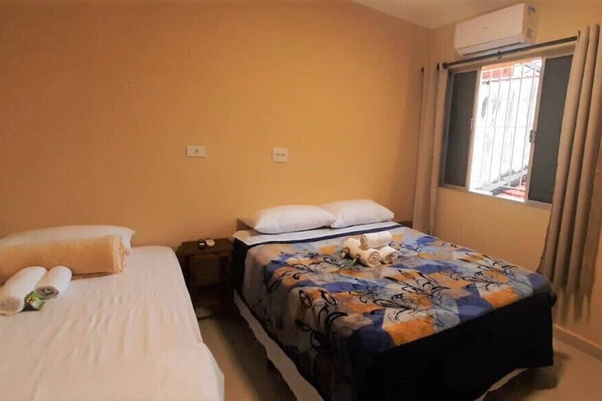 A hotel room with two beds, a window with curtains, and an air conditioning unit.