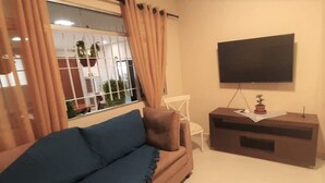A living room with a sofa, a TV on the wall, a small table with a plant, and a window with curtains. - Hostel B2B (São Paulo)