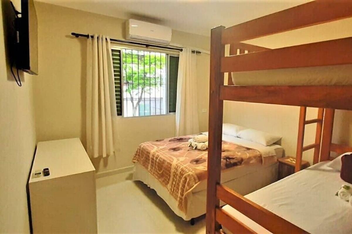 A compact room with two bunk beds, a small bedside table, a window with curtains, and a wall-mounted TV.