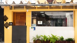 A yellow building with a wooden door marked '176', a window with a sign, and a small fence with plants. - Hostel B2B (São Paulo)