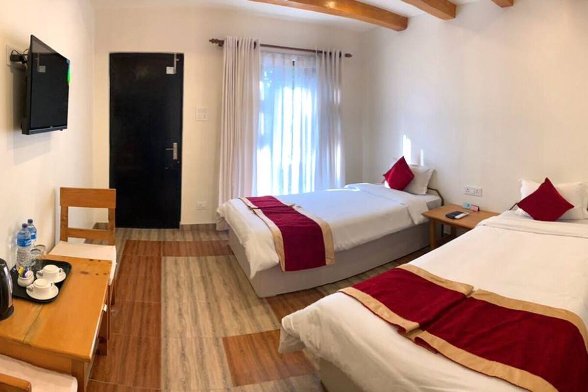 A hotel room with two beds, a wooden desk, a television, and a door.