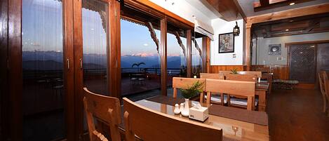 A wooden interior with a dining area, large windows, and a view of mountains.