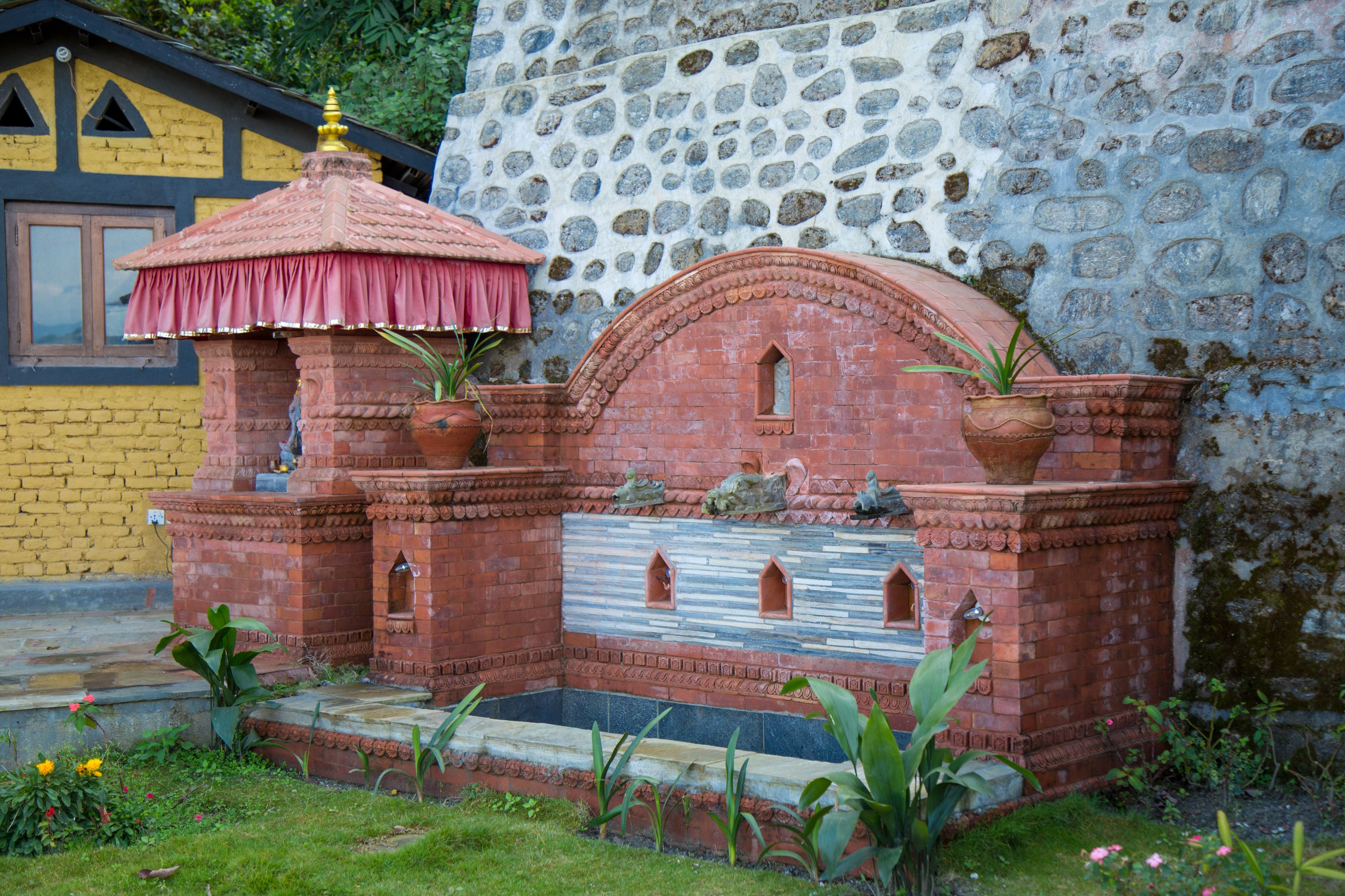 A small brick structure with a tiled roof, a stone wall, and potted plants.
