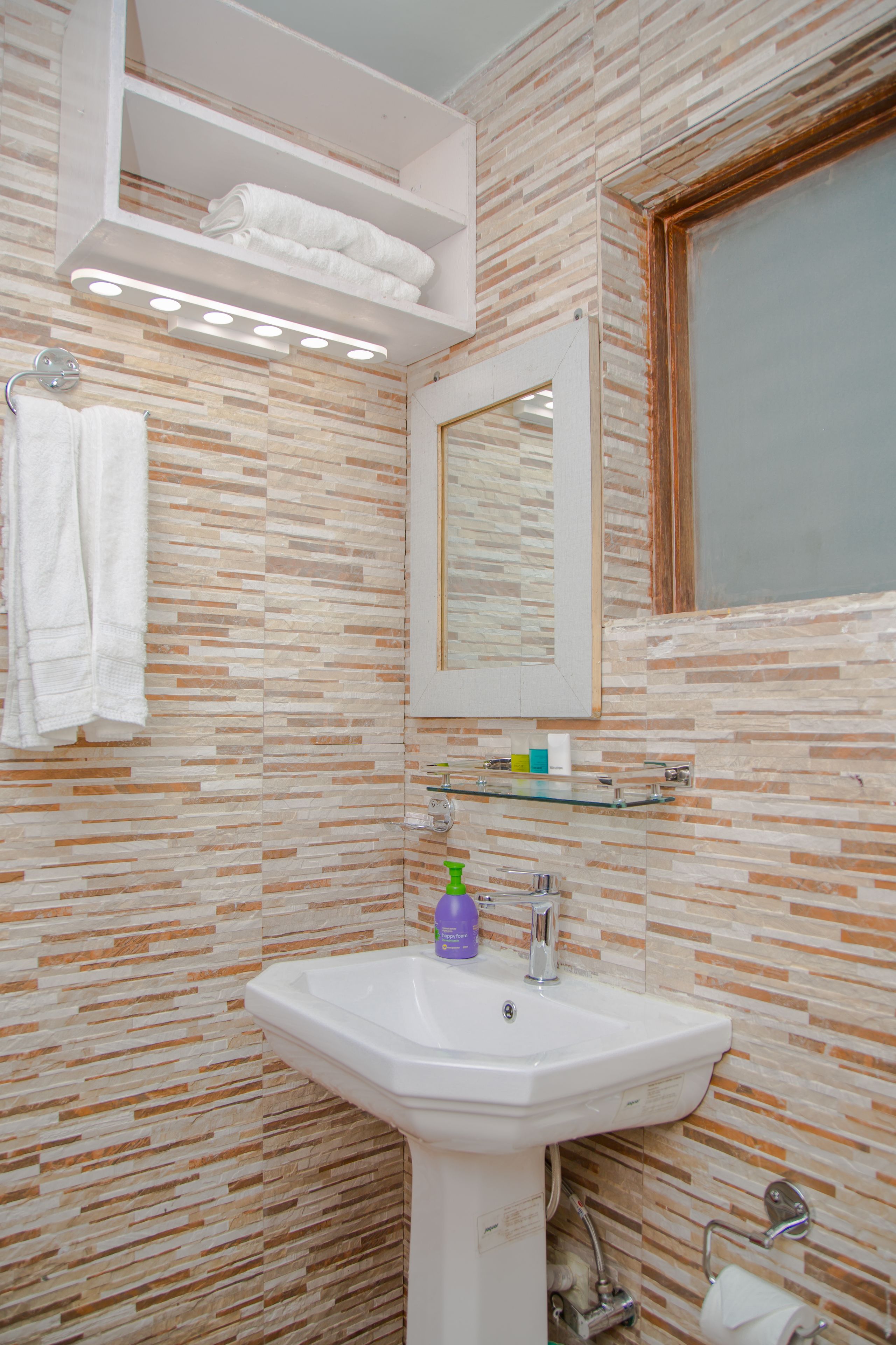 A bathroom with a tiled wall, a white sink, a mirror, and a towel rack.