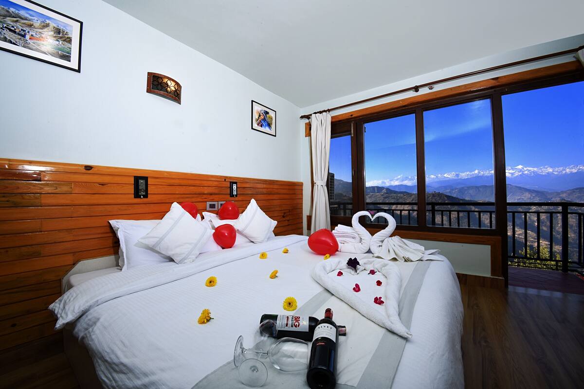 A hotel room with a bed, a window with a mountain view, and a bottle of wine on the bed.