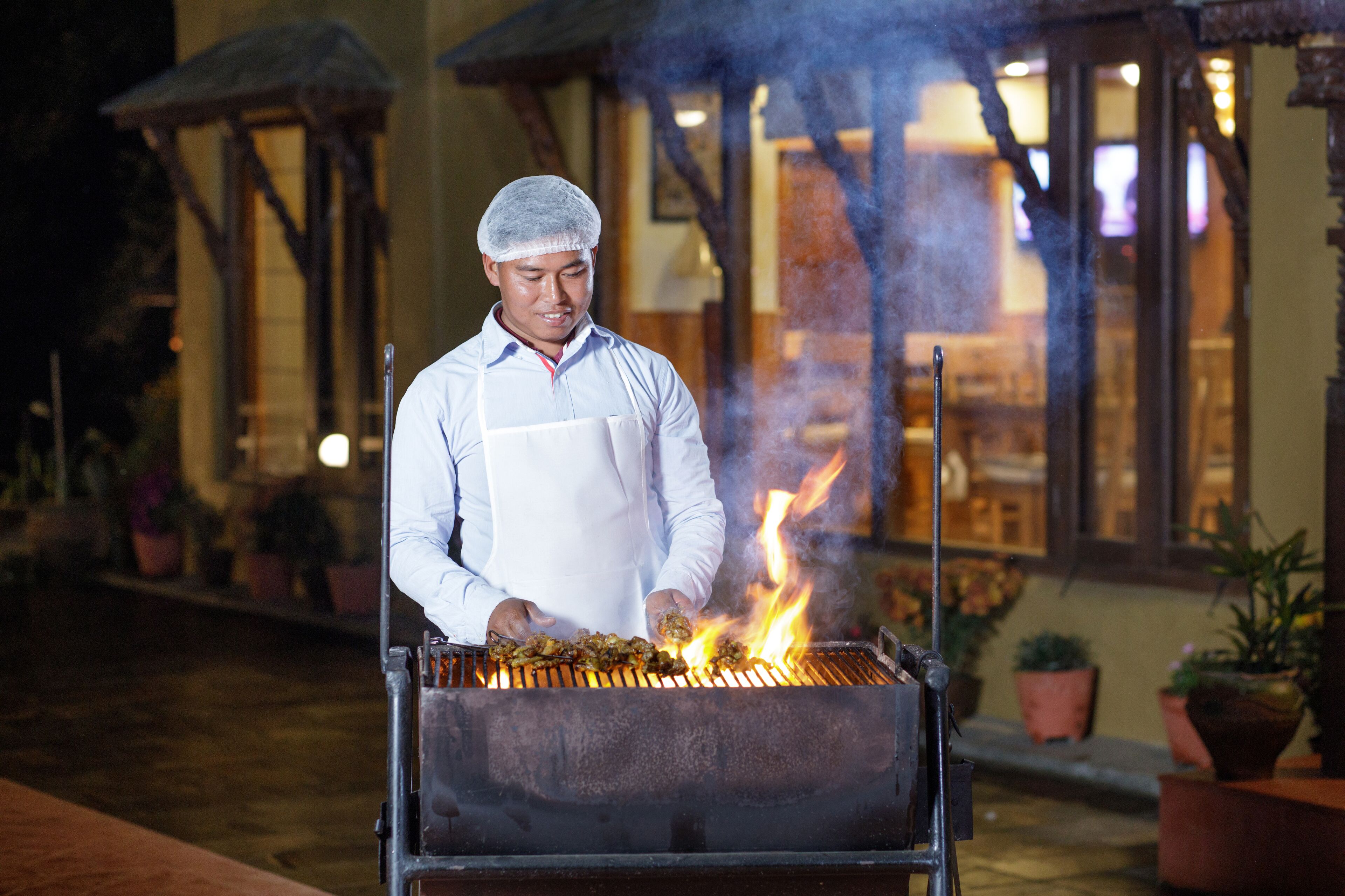 Ein Koch grillt im Freien, im Hintergrund ist ein Gebäude zu sehen.