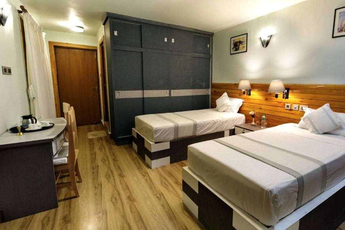A room with two single beds, a wooden headboard, a desk with a chair, and a wardrobe.